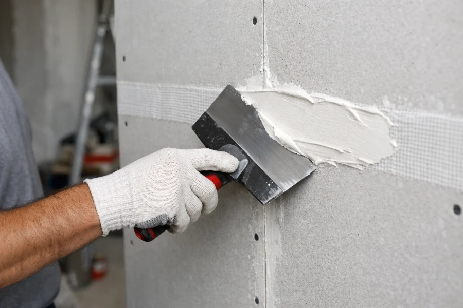 Installer applying joint compound over fiberglass mesh tape on magnesium oxide (MgO) board seams with a taping knife